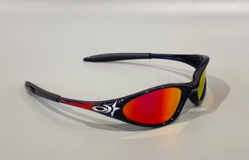 May include: Sport sunglasses with a black frame, red and yellow gradient lenses, and a white star design. The arms have red accents. These sunglasses are designed for outdoor activities and offer UV protection.