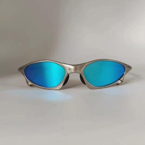 May include: Silver-framed sunglasses with vibrant blue lenses. The oval-shaped lenses reflect a bright, mirrored finish. The sunglasses have a sleek, modern design, suitable for outdoor activities.