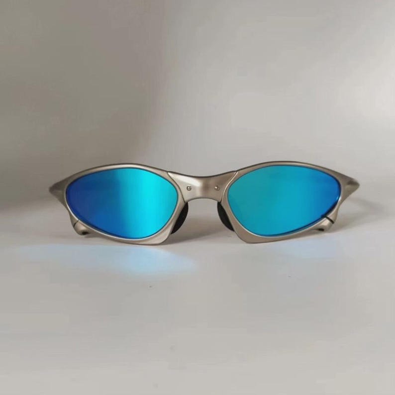 May include: Silver-framed sunglasses with vibrant blue lenses. The oval-shaped lenses reflect a bright, mirrored finish. The sunglasses have a sleek, modern design, suitable for outdoor activities.