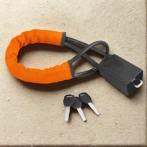 Könnte beinhalten: Ein orangefarbenes Fahrradschloss mit schwarzem Verschlussmechanismus und drei Schlüsseln. Das Schloss hat eine dicke, gepolsterte orangefarbene Hülle und ein schwarzes Kabel. Die Schlüssel sind silber und schwarz.