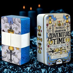 May include: A deck of tarot cards wrapped in a white paper band and a rectangular metal tin featuring the text A TOTALLY UNOFFICIAL ADVENTURE TIME TAROT DECK BY KATHERINE HILLIER, decorated with cartoon illustrations of swords, cups, and characters.