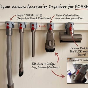 May include: A grey plastic vacuum accessory organiser mounted on a white wall rail, designed for 60cm and 80cm frames. It features five sliding mounts with red release buttons to hold various Dyson vacuum attachments securely in place.