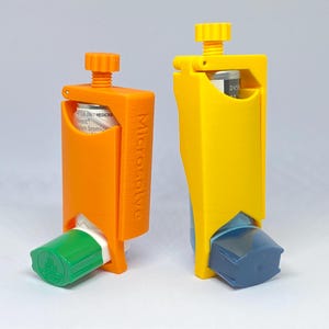 Puede incluir: Dos dispositivos inhaladores, uno naranja y otro amarillo, con un cartucho cilíndrico visible en el interior. El dispositivo naranja tiene una boquilla verde, y el amarillo una boquilla azul. Ambos tienen un mecanismo de rosca. El dispositivo naranja tiene la palabra "Microsolve".