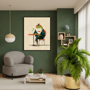 Puede incluir: Una impresión artística enmarcada representa una rana con esmoquin sentada a una mesa con un martini. La rana lleva un sombrero de copa y una pajarita. El fondo es de color beige neutro y la mesa es roja.