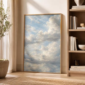 Könnte beinhalten: Ein rechteckiger Wandkunstdruck mit einem detaillierten Gemälde eines hellblauen Himmels voller weicher, weißer und hellgrauer Kumuluswolken. Das Kunstwerk ist in einen dünnen, hellen Holzrahmen gefasst und zeigt eine ruhige atmosphärische Szene.
