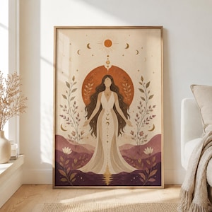 Op de afbeelding: Een verticale wandkunstprint met een centrale figuur met lang donker haar in een vloeiende crèmekleurige jurk. De illustratie bevat een grote oranje zon, hemelse maanfasen en gestileerde botanische elementen in tinten bruin en paars.