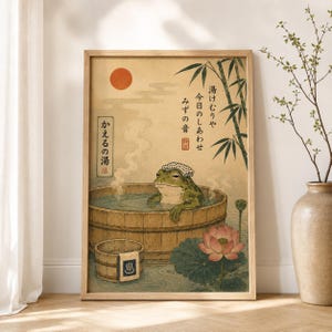 K&ouml;nnte beinhalten: Ein gerahmter Kunstdruck mit einem gr&uuml;nen Frosch, der ein wei&szlig;es Handtuch auf dem Kopf tr&auml;gt und in einem Holzzuber badet. Das Bild zeigt eine rote Sonne, Bambus, eine Lotusbl&uuml;te und japanischen Text auf einem Hintergrund in gealterter Papieroptik.
