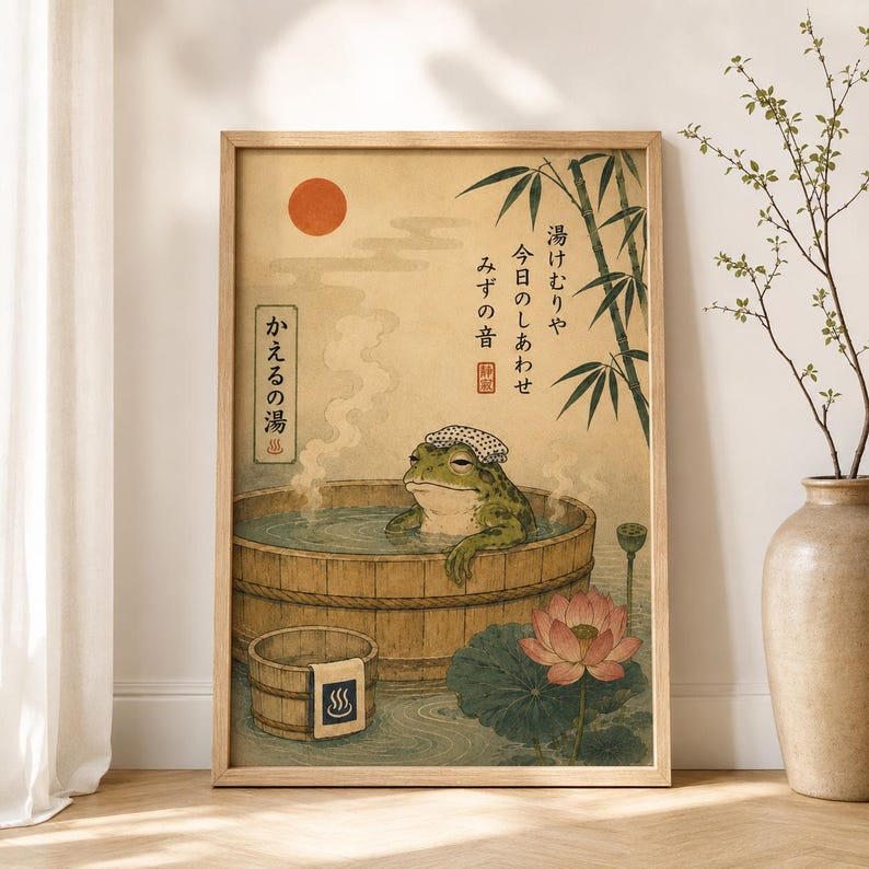 K&ouml;nnte beinhalten: Ein gerahmter Kunstdruck mit einem gr&uuml;nen Frosch, der ein wei&szlig;es Handtuch auf dem Kopf tr&auml;gt und in einem Holzzuber badet. Das Bild zeigt eine rote Sonne, Bambus, eine Lotusbl&uuml;te und japanischen Text auf einem Hintergrund in gealterter Papieroptik.