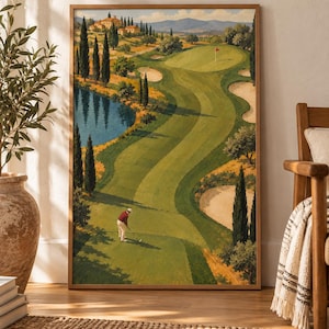 May include: A framed landscape painting depicting a golf course with a golfer in a red shirt and white trousers standing on a green fairway. The scene includes a blue pond, tall cypress trees, sand bunkers, and a distant villa under a clear sky.