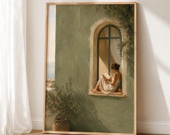 May include: A framed wall art print depicting a person in a light-coloured dress sitting on a window ledge reading a book. The scene features a textured sage green wall, an arched window frame, a potted olive tree, and a glimpse of a distant sea.