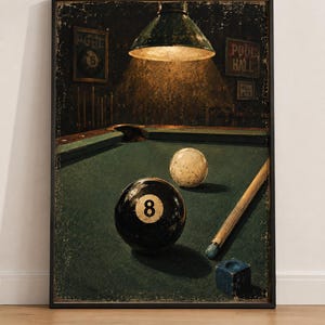 Può includere: Una stampa artistica incorniciata che raffigura una sala da biliardo con un tavolo dal panno verde, una palla nera numero 8, una palla bianca, una stecca in legno e un cubetto di gesso blu. Una lampada sospesa illumina il tavolo dall'alto.