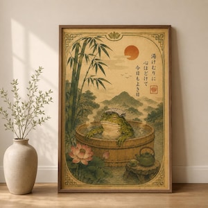 May include: A framed wall art print featuring a green frog relaxing in a wooden hot tub with steam rising. The scene includes bamboo stalks, a lotus flower, a small teapot, and Japanese text. The background shows mountains and a red sun.