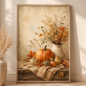 May include: A framed wall art print depicting a still life scene with a large orange pumpkin, smaller gourds, a pear, and an apple arranged on a plaid cloth. A white ceramic pitcher holds a bouquet of dried autumn leaves and golden foliage.