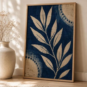 Può includere: Un'opera d'arte da parete rettangolare incorniciata con una stampa botanica blu intenso su uno sfondo in tessuto beige testurizzato. Il design mostra un ramo centrale con foglie affiancato da due motivi circolari parziali composti da piccoli punti blu.