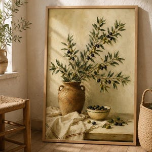 Könnte beinhalten: Ein gerahmter Kunstdruck, der ein Stillleben mit einer rustikalen braunen Keramikvase voller Olivenzweige, einer kleinen Schale mit Oliven und verstreuten Oliven auf einem drapierten weißen Tuch vor einem strukturierten hellgelben Hintergrund zeigt.