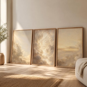Peut inclure: Un ensemble de trois impressions d'art mural rectangulaires verticales représentant des formations nuageuses douces et éthérées dans des tons crème, beige et or pâle. Chaque impression est encadrée de bois clair, formant un ciel continu.