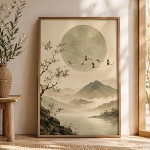 May include: A framed rectangular wall art print featuring a landscape scene with a large pale moon, a flock of birds in flight, layered mountain ranges, a calm body of water, and a tree on a rocky cliffside, all rendered in muted beige and gray tones.