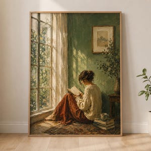 May include: A framed wall art print depicting a person sitting on the floor by a large window, reading a book. The person wears a cream-colored sweater and a long rust-colored skirt. The room features green walls, a small side table, and books.