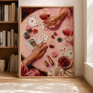 Peut inclure: Une peinture à l'huile encadrée représentant une table rose avec des cartes à jouer, des dés rouges, des jetons de poker, deux verres à martini remplis de liquide rouge et de cerises, un rouge à lèvres doré et un bol de cerises.
