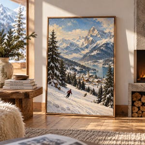 May include: A framed wall art print depicting a snowy mountain landscape with a village near a lake. The scene features evergreen trees covered in snow, two skiers on a slope, and jagged, snow-capped peaks under a bright blue sky with clouds.