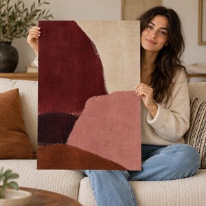 May include: A rectangular art print featuring an abstract composition of layered organic shapes in deep burgundy, muted pink, dark purple, and earthy brown against a textured beige background, printed on a canvas-like material with visible weave.