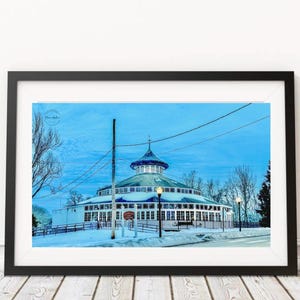 May include: A framed print of a round building with a blue roof and white walls, set against a blue sky. The building has multiple windows and is surrounded by snow. Power lines and streetlights are visible.