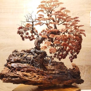 Peut inclure: Sculpture d'arbre bonsaï en fil de cuivre avec un tronc torsadé et des branches détaillées. L'arbre présente des feuilles brun rougeâtre et est monté sur une base en bois brun foncé texturé. La sculpture est exposée sur un socle en bois.