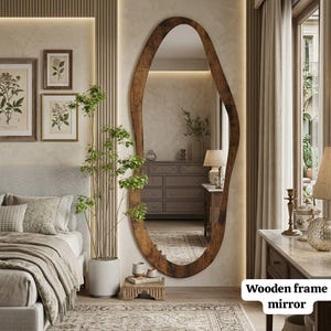 May include: A full-length floor mirror featuring an irregular, organic-shaped wooden frame with a dark brown finish. The mirror is mounted against a wall, reflecting a bedroom interior with a dresser, a lamp, and a potted plant.
