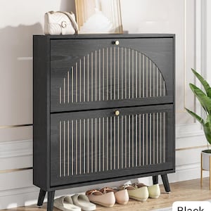 May include: Black shoe cabinet with two compartments, each with a door featuring vertical and arched gold-colored accents. The cabinet has gold knobs and sits on four angled legs. Several pairs of shoes are visible at the base.