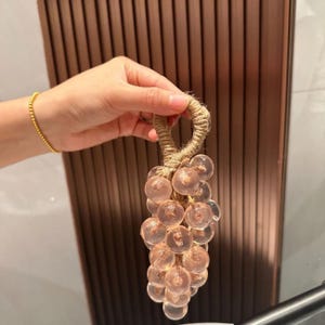 Peut inclure: Un groupe de raisins décoratifs en verre transparent, teinté de rose, avec une poignée en corde de jute. Les sphères de verre sont regroupées, créant un design unique. La poignée est en corde de jute naturelle. Cet article convient à la décoration intérieure.