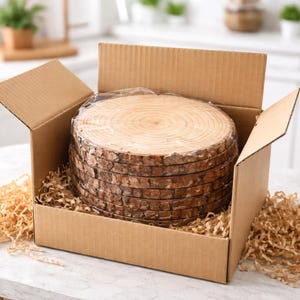 May include: A stack of natural wood slices, each approximately 6 inches in diameter, packaged in a cardboard box with protective packing material. The wood slices have visible growth rings and bark edges, suggesting a rustic, handcrafted aesthetic.