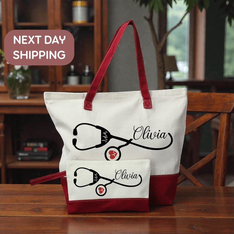 A red and white tote bag with a stethoscope design and the name "Olivia" printed on it, along with a smaller white bag with the same design and name. The bag is placed on a wooden surface, and there is a "Next Day Shipping" sign in the background.