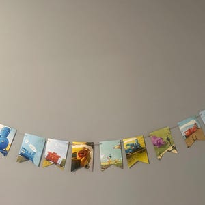 May include: A banner of vintage book pages, each cut into a pennant shape and strung together. The illustrations depict colorful trains and scenes, creating a whimsical and nostalgic decoration. The banner is suspended against a neutral wall.