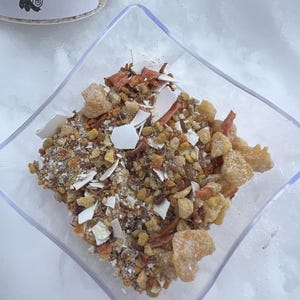 May include: A clear glass bowl filled with a mixture of dried fruit, herbs, and other ingredients. The ingredients are a mix of light brown, orange, and white.
