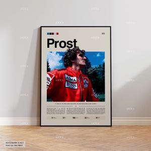 May include: A framed poster featuring a portrait of Alain Prost in a red racing suit. The poster includes the name "Prost" in large letters, along with the text "AIMA BOSS" and other details. The background is a light beige colour.