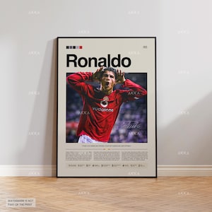 Puede incluir: Un póster enmarcado con una fotografía de Cristiano Ronaldo con una camiseta roja. El póster incluye el nombre "Ronaldo" en letras negras grandes, una firma y el logotipo de Vodafone. El póster tiene un fondo beige y un marco negro.