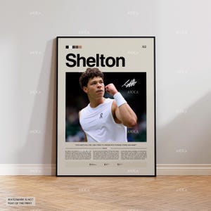 Op de afbeelding: Een ingelijste poster met de naam "Shelton" in grote zwarte letters. De poster toont een foto van een tennisser in een witte tanktop en polsband. Het ontwerp heeft een neutraal kleurenschema met een beige achtergrond en een zwart frame.