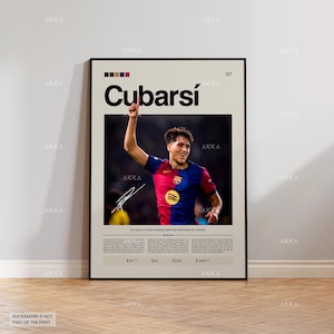 May include: A framed poster with the name "Cubarsí" in large black letters. The poster features a photograph of a footballer in a red and blue jersey with his arm raised. The poster has a beige background and a black frame.