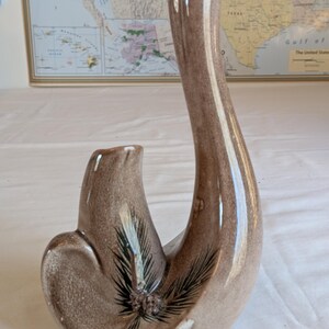 May include: A brown ceramic vase with a curved, organic shape. The vase features a tall, slender neck and a rounded base with a decorative pine needle design. The vase has a glossy finish.