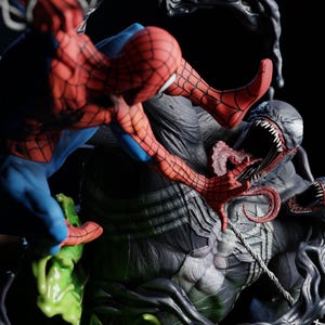 May include: A detailed figurine depicting Spider-Man in a dynamic pose, battling Venom. Spider-Man is in his classic red and blue suit, while Venom is a large, dark figure with a menacing expression. The base features green and black elements.