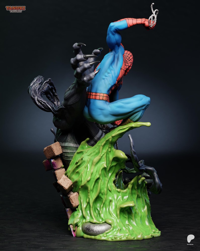 May include: A detailed figurine of Spider-Man in a dynamic pose, clad in his signature blue and red suit. He is perched atop a vibrant green, textured base, with a dark, clawed figure reaching towards him. The figurine has the Tanuki Figures logo.