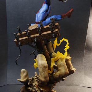 May include: A detailed figurine of Spider-Man in a dynamic pose, clad in his signature blue and red suit. He is suspended mid-air, seemingly swinging from a wooden structure with electrical components. The base features a textured, organic design with yellow lightning effects.