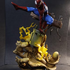 May include: A detailed figurine of Spider-Man in a dynamic pose, clad in his signature red and blue suit. The figure is perched on a detailed base with electrical components and stylized yellow lightning effects, showcasing a comic book theme.