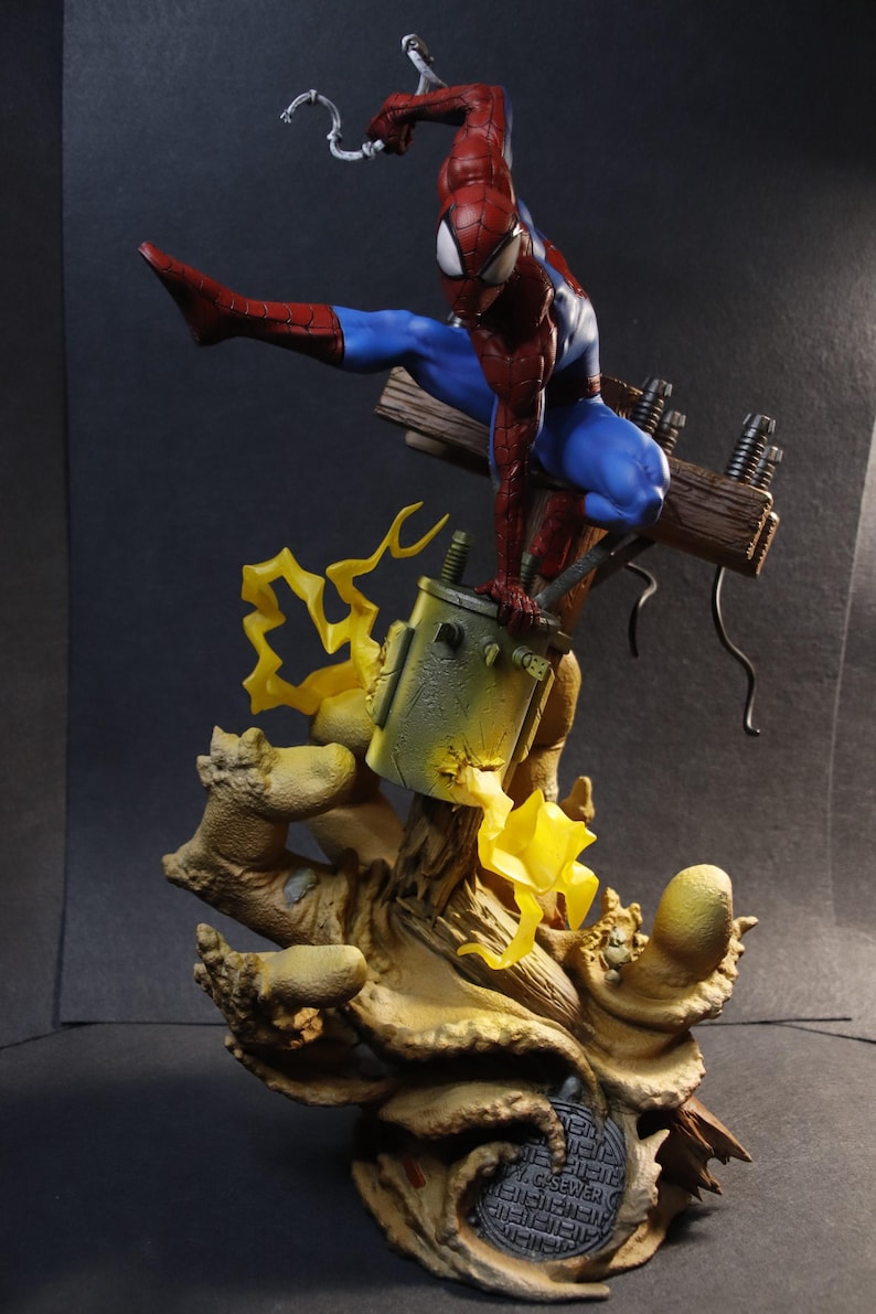 May include: A detailed figurine of Spider-Man in a dynamic pose, clad in his signature red and blue suit. The figure is perched on a detailed base with electrical components and stylized yellow lightning effects, showcasing a comic book theme.