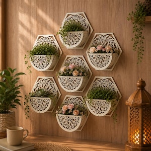 Può includere: Un set di sette fioriere esagonali da parete realizzate in legno chiaro con intricati motivi geometrici tagliati al laser. Ogni fioriera presenta un bacino semicircolare contenente varie piante verdi e piccoli fiori rosa e bianchi.