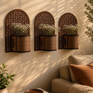 Peut inclure: Trois jardinières murales décoratives en bois brun foncé, chacune avec un cadre en forme d'arche et un contenant en forme de panier tressé. Elles contiennent de petites fleurs blanches. Elles sont fixées sur un mur beige.