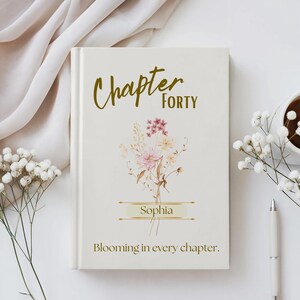 以下が含まれることがあります： クリーム色の本で、金色の筆記体で「Chapter Forty」と書かれています。 下にはピンクとクリーム色の花束があり、その下に「Sophia」という名前があります。 下部には「Blooming in every chapter」というフレーズがあります。