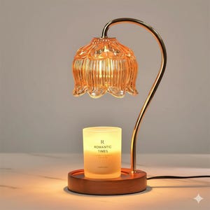 Könnte beinhalten: Ein dekorativer Kerzenwärmer mit einem goldfarbenen, gebogenen Arm, der einen blütenförmigen, bernsteinfarbenen Glasschirm trägt. Eine brennende Kerze steht auf einem Holzsockel, mit dem Text "R ROMANTIC TIMES" sichtbar.