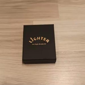 Puede incluir: Una caja rectangular negra con acabado mate. Centrada en la tapa est&aacute; la palabra LIGHTER impresa en letras may&uacute;sculas doradas, con el texto High-Grade impreso en letras doradas m&aacute;s peque&ntilde;as debajo, flanqueado por dos l&iacute;neas doradas horizontales.