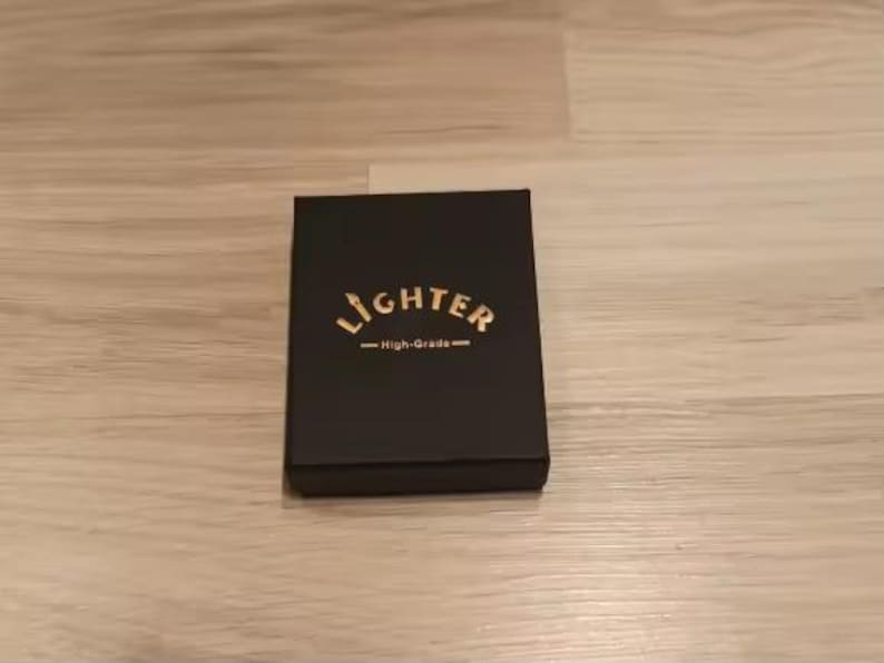 Puede incluir: Una caja rectangular negra con acabado mate. Centrada en la tapa est&aacute; la palabra LIGHTER impresa en letras may&uacute;sculas doradas, con el texto High-Grade impreso en letras doradas m&aacute;s peque&ntilde;as debajo, flanqueado por dos l&iacute;neas doradas horizontales.